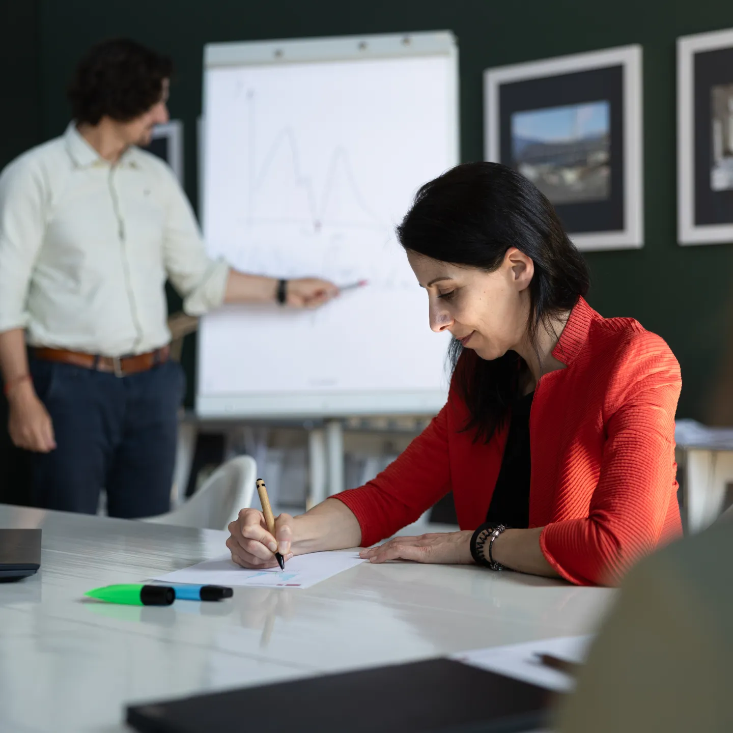Dozent präsentiert mathematische Funktion an Flipchart, während eine Teilnehmerin aktiv mitschreibt.