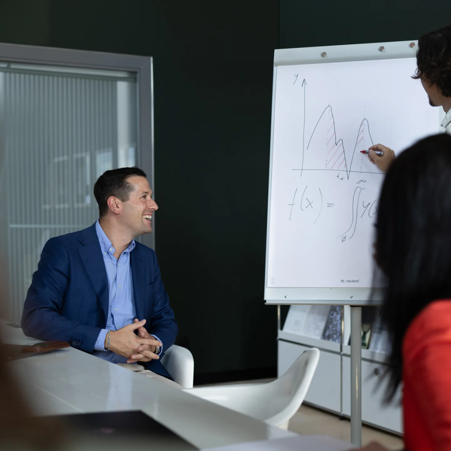 Teilnehmende bei einer Präsentation im Seminarraum, Fokus auf Vortragendem und Flipchart mit Funktionsgleichung.