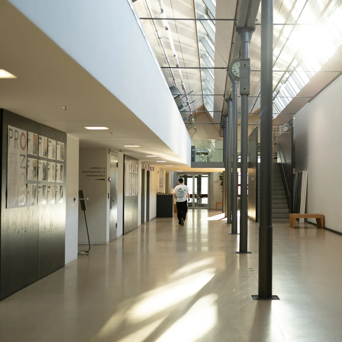 Heller Flur mit Uhr, Sitzgelegenheiten und Zugang zu Hörsälen an der Universität Liechtenstein.