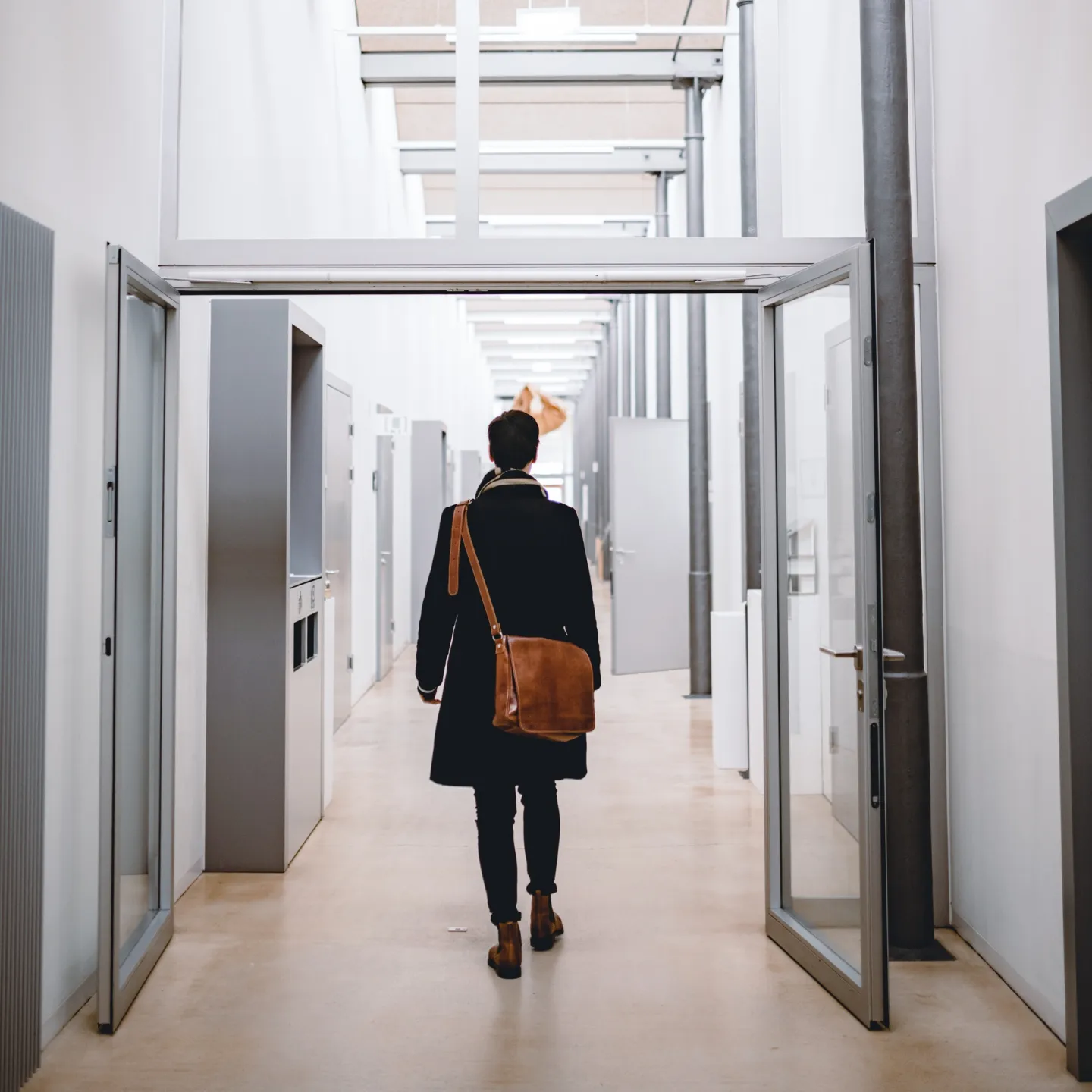 Studierende*r durchquert lichtdurchfluteten Hochschulflur der Universität Liechtenstein mit Dialektschrift an der Decke – modernes Campusambiente mit regionalem Bezug.