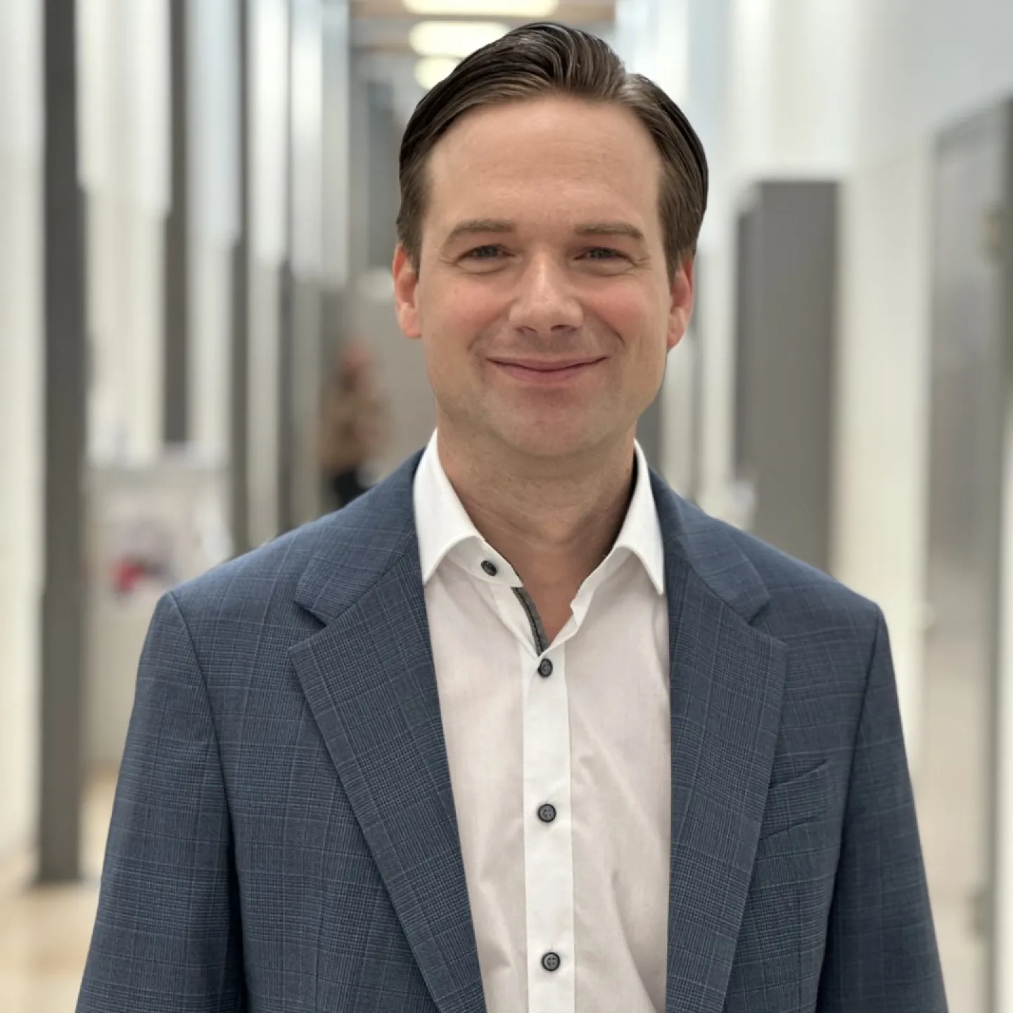 Ein lächelnder Mann in einem blauen Anzug steht in einem modernen, hellen Flur.