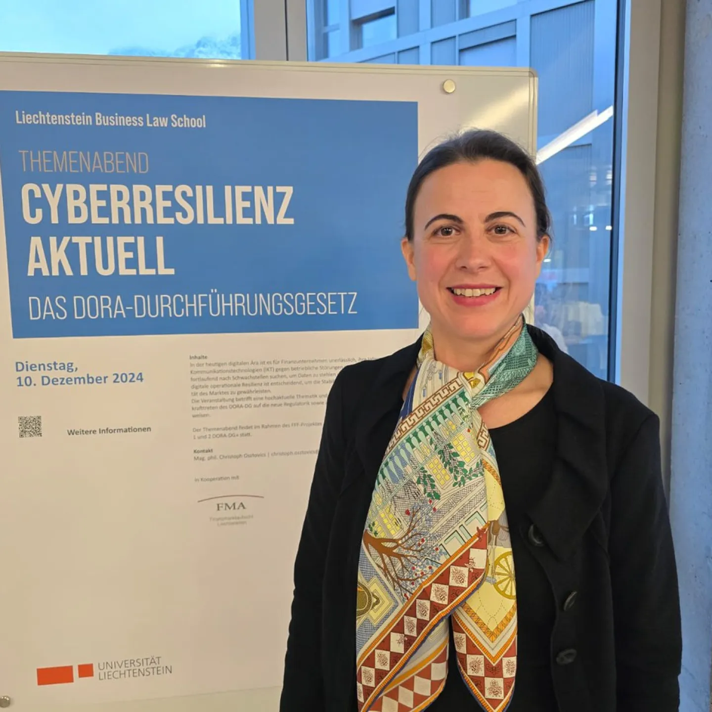 Frau steht lächelnd vor einem Plakat der Liechtenstein Business Law School. Das Plakat kündigt den Themenabend „Cyberresilienz aktuell: Das DORA-Durchführungsgesetz“ an, der am 10. Dezember 2024 stattfindet.
