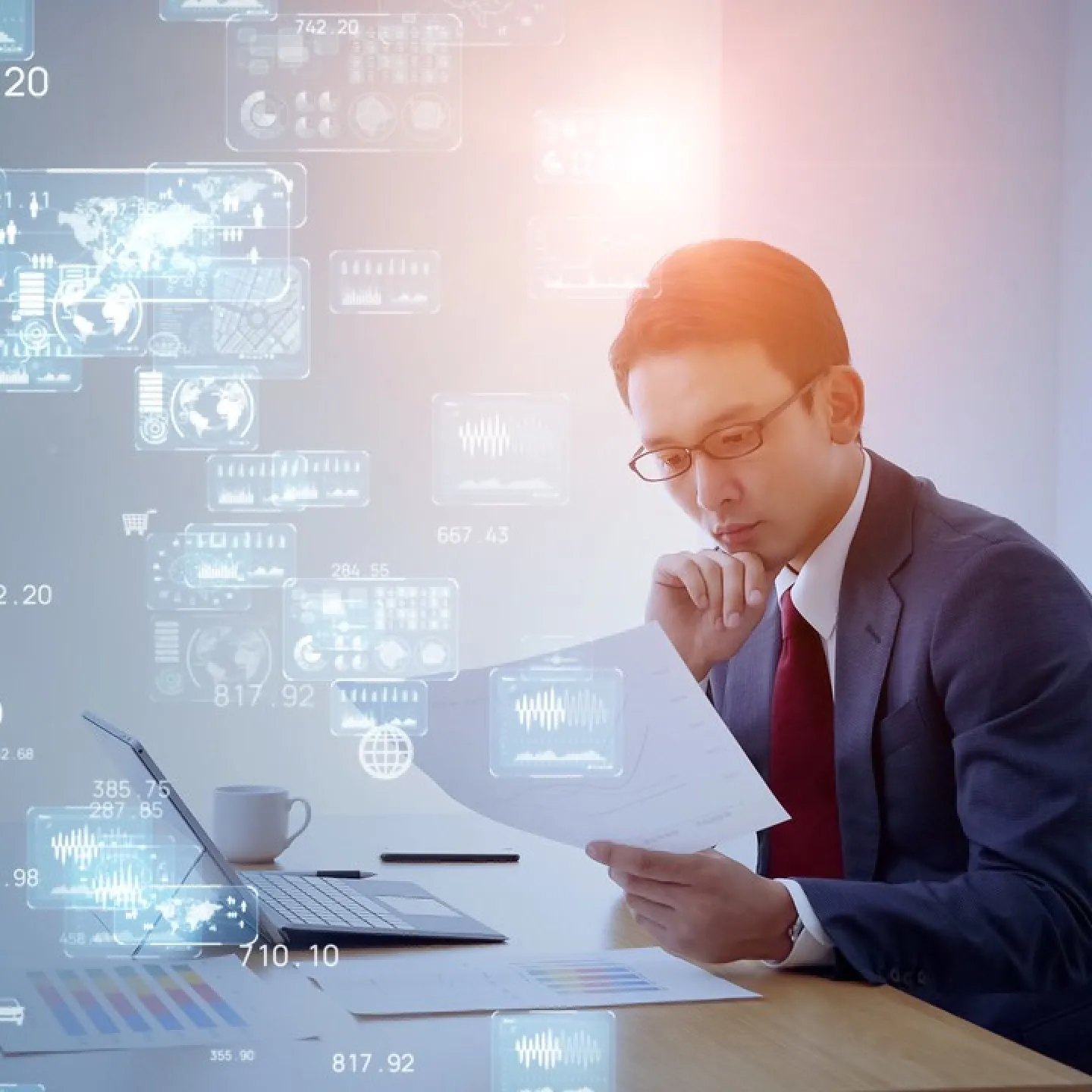 Ein Mann im Anzug sitzt an einem Schreibtisch und betrachtet konzentriert Dokumente. Vor ihm steht ein Laptop, umgeben von digitalen Grafiken und Datenvisualisierungen, die den digitalen Wandel symbolisieren.