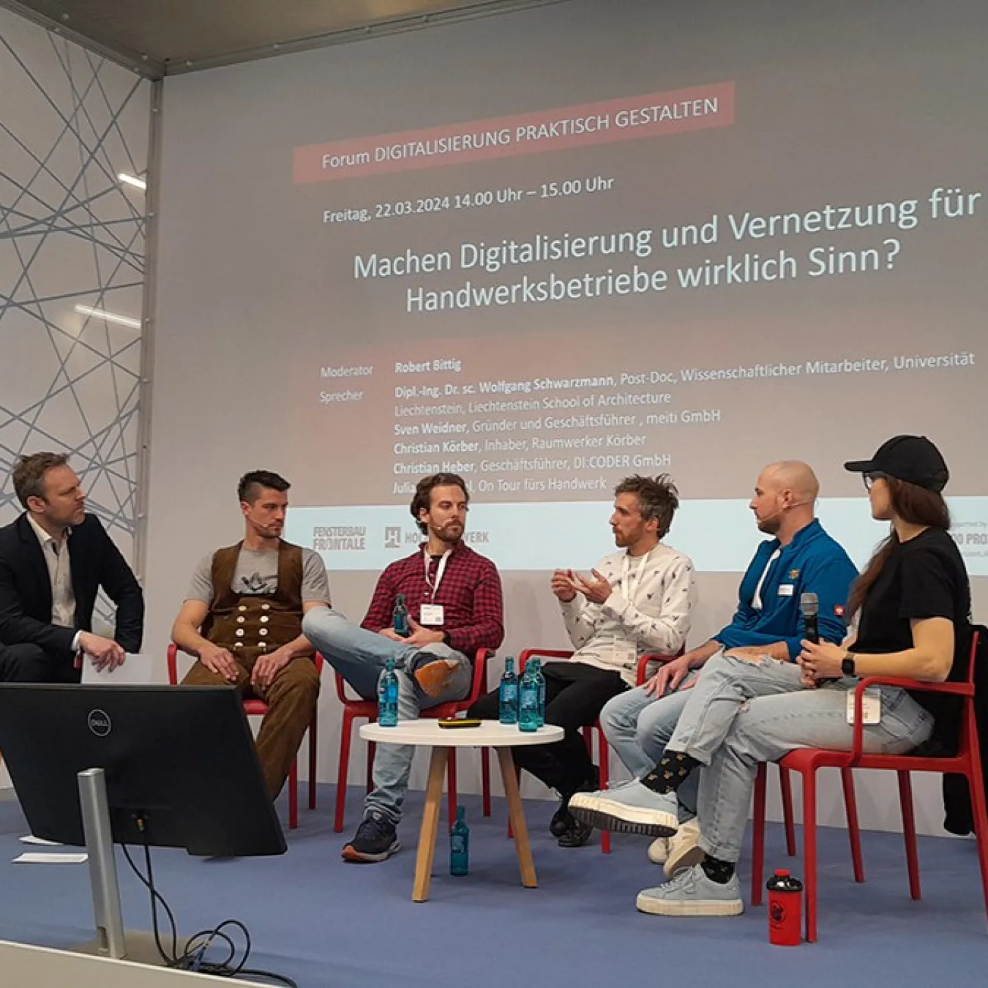 Podiumsdiskussion auf der Messe «Holz Handwerk 2024» in Nürnberg. Fünf Personen sitzen auf einer Bühne vor einer Leinwand mit dem Titel "Machen Digitalisierung und Vernetzung für Handwerksbetriebe wirklich Sinn?". Die Diskussion thematisiert die Rolle der Digitalisierung im Handwerk.