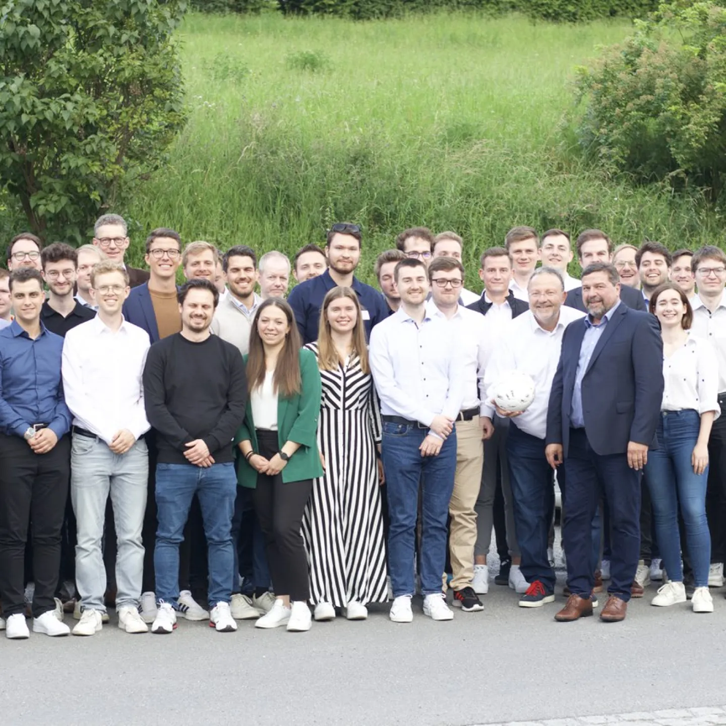 Gruppe von Doktoranden und Professoren steht lächelnd vor einer grünen Wiese bei der Universität Liechtenstein während des Internationalen Doktorandenseminars 2024.