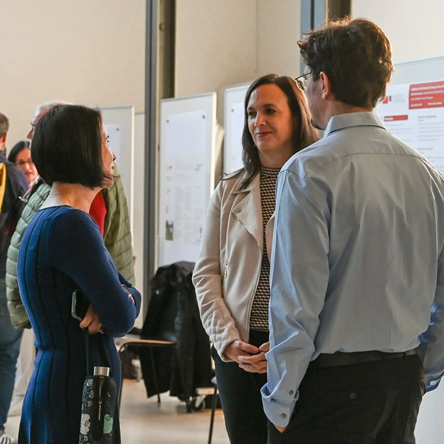 Menschen stehen in einem Auditorium der Universität Liechtenstein und unterhalten sich vor Ausstellungstafeln. Die Atmosphäre ist lebhaft, und die Veranstaltung scheint gut besucht zu sein.