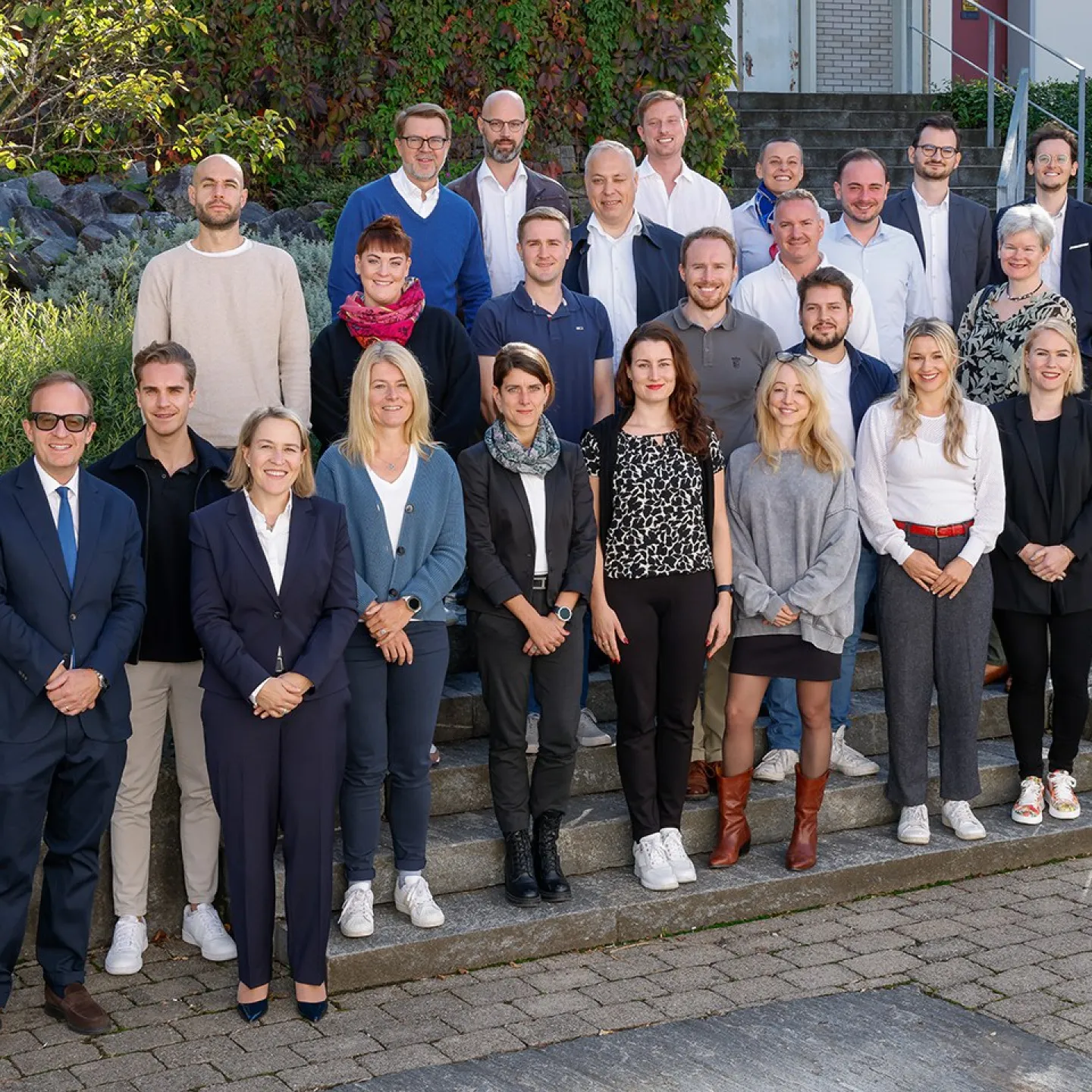 Gruppenfoto von Studierenden und Dozenten des Executive Master of Laws (LL.M.) im Gesellschafts-, Stiftungs- und Trustrecht an der Universität Liechtenstein. Die Gruppe steht auf einer Treppe im Freien, umgeben von grüner Vegetation.