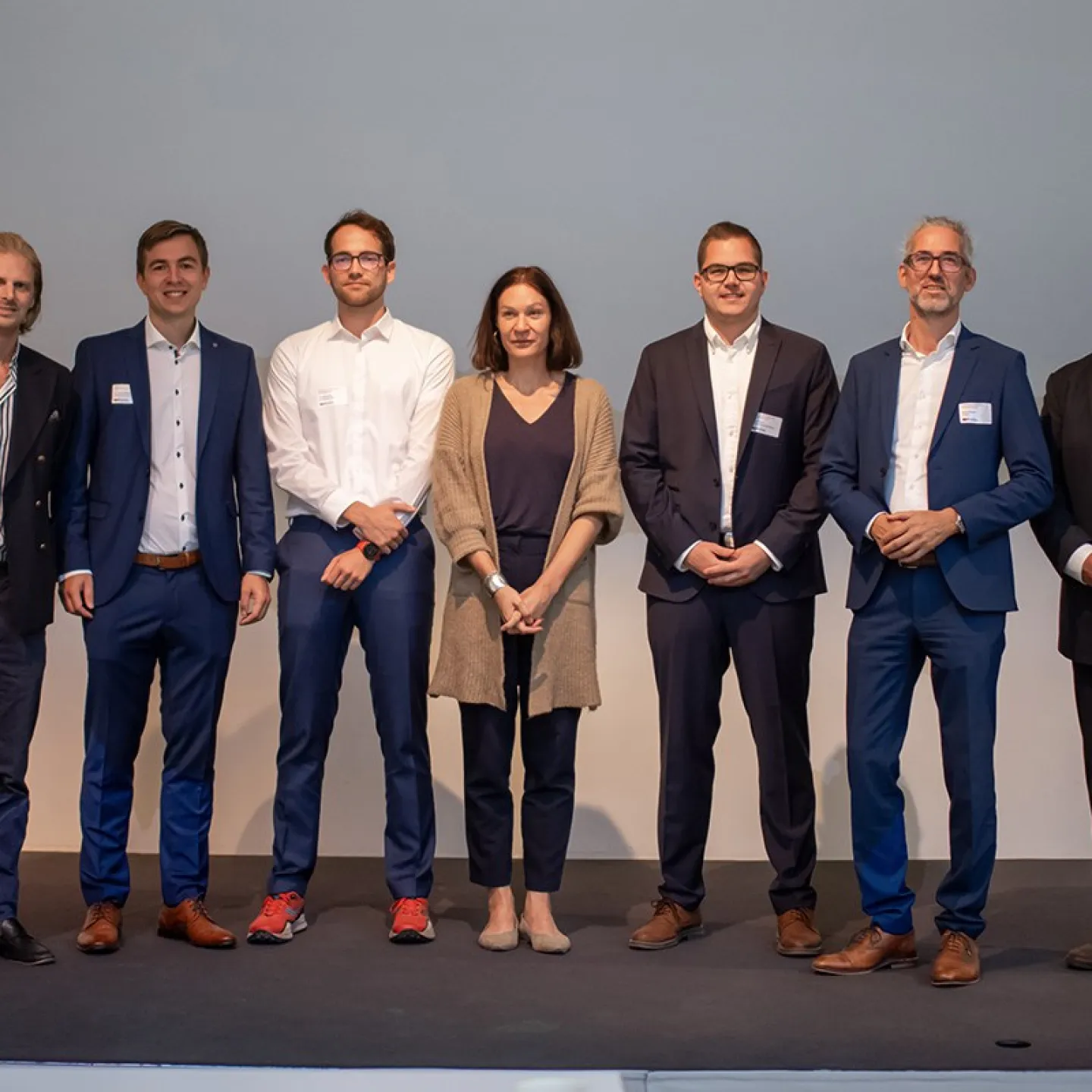 Eine Gruppe von sieben Personen steht auf einer Bühne beim 8. Liechtenstein Workshop of Sustainable Finance an der Universität Liechtenstein. Sie tragen formelle Kleidung und lächeln in die Kamera.