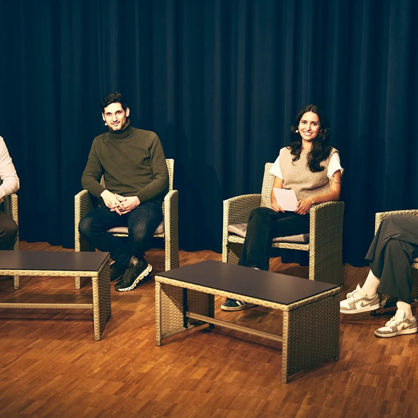 Vier Personen sitzen auf einer Bühne in Korbstühlen, vor einem dunklen Vorhang. Sie sind Teil einer Diskussionsrunde über Upcycling in der Architektur an der Universität Liechtenstein.