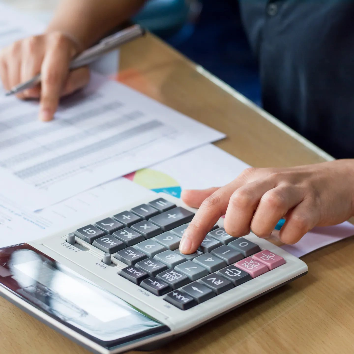 Person sitzt am Tisch mit Taschenrechner und Papier und rechnet