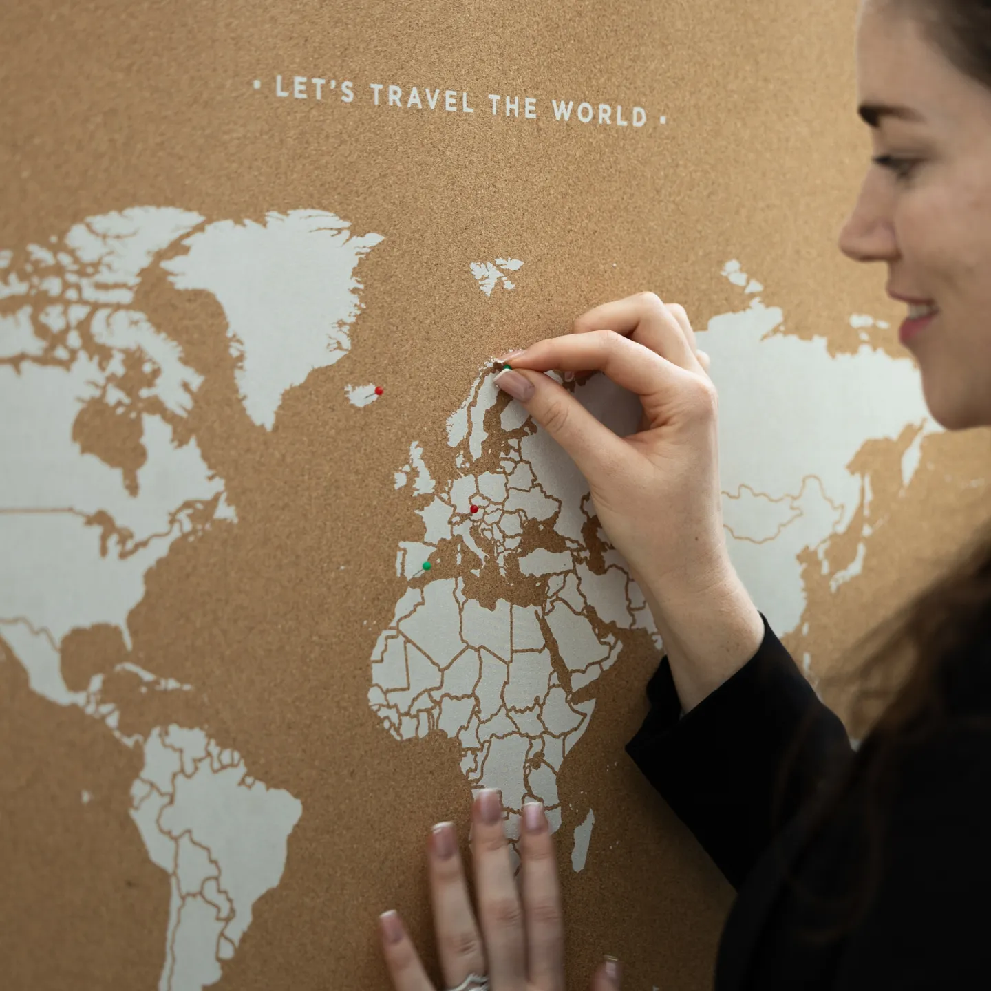 Frau steckt roten Pin in Weltkarte mit Aufschrift „Let’s Travel the World“.