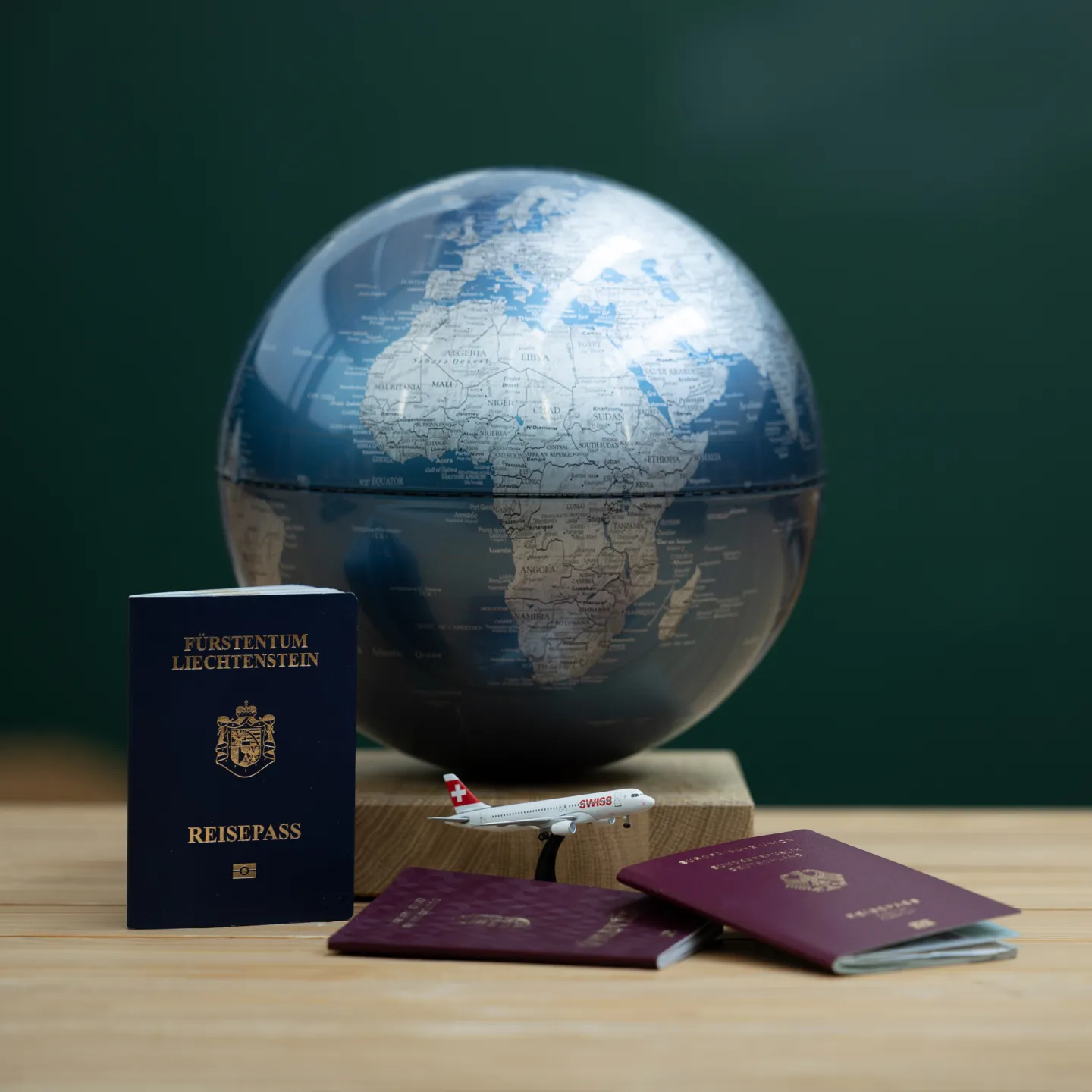 Globus mit Reisepässen aus Liechtenstein und EU sowie Modellflugzeug auf Tisch.