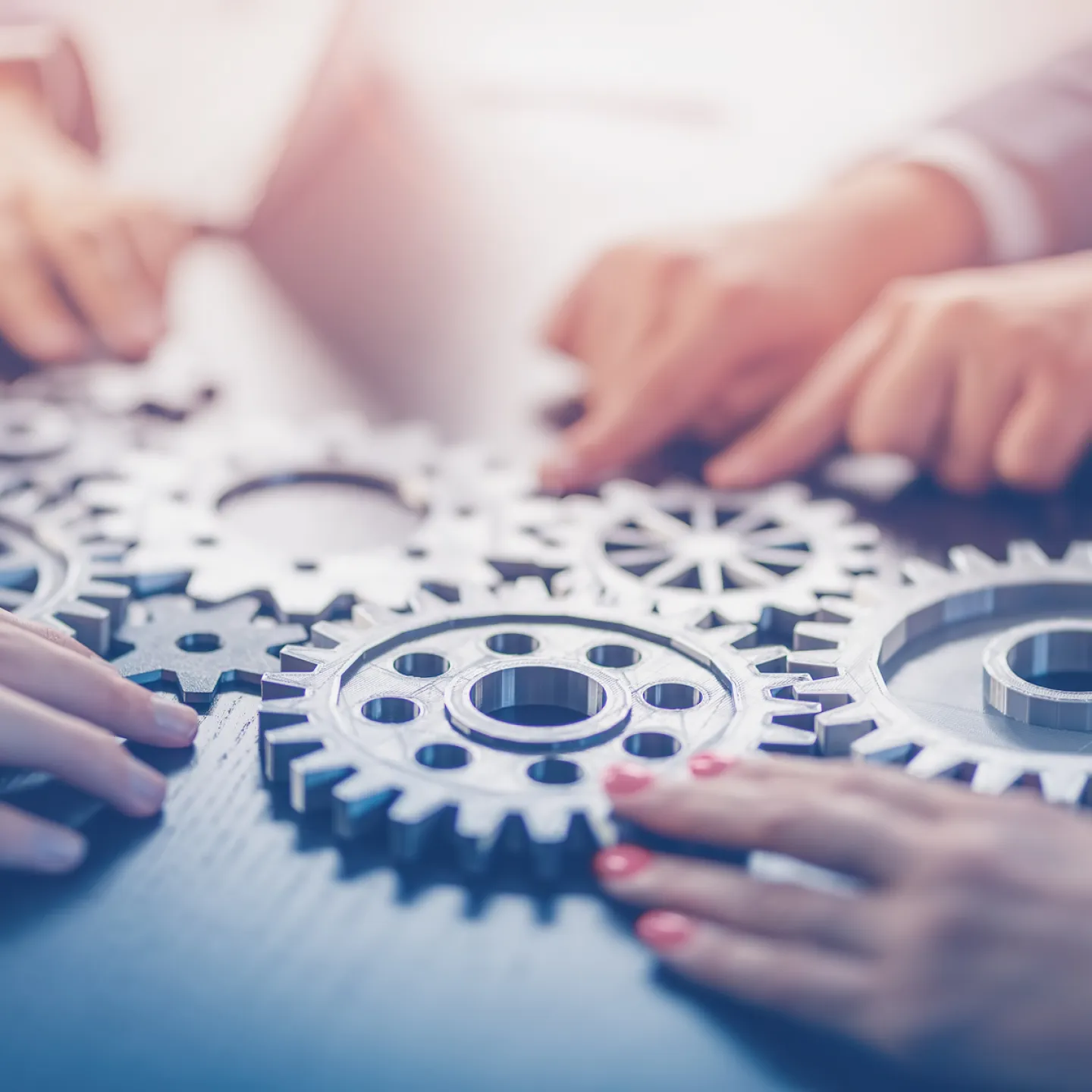 Mehrere Hände halten verzahnte Zahnräder als Symbol für Teamarbeit und Kooperation.