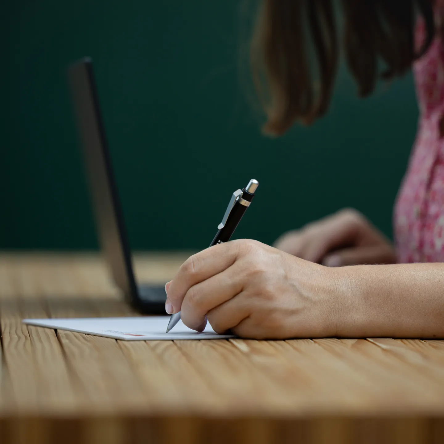 Person schreibt mit Stift auf Papier vor Laptop im Arbeitsraum der Universität Liechtenstein.