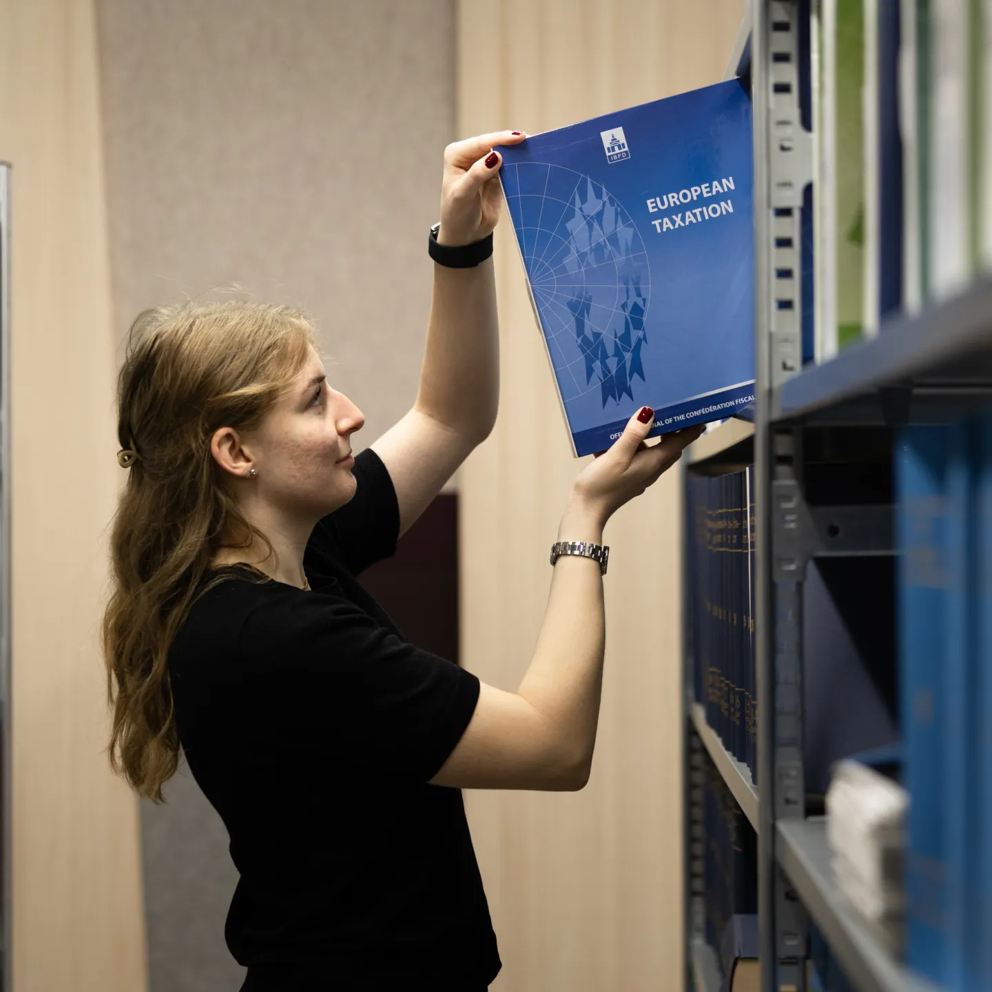 Frau holt Zeitschrift European Taxation aus Regal in der Bibliothek der Universität Liechtenstein.
