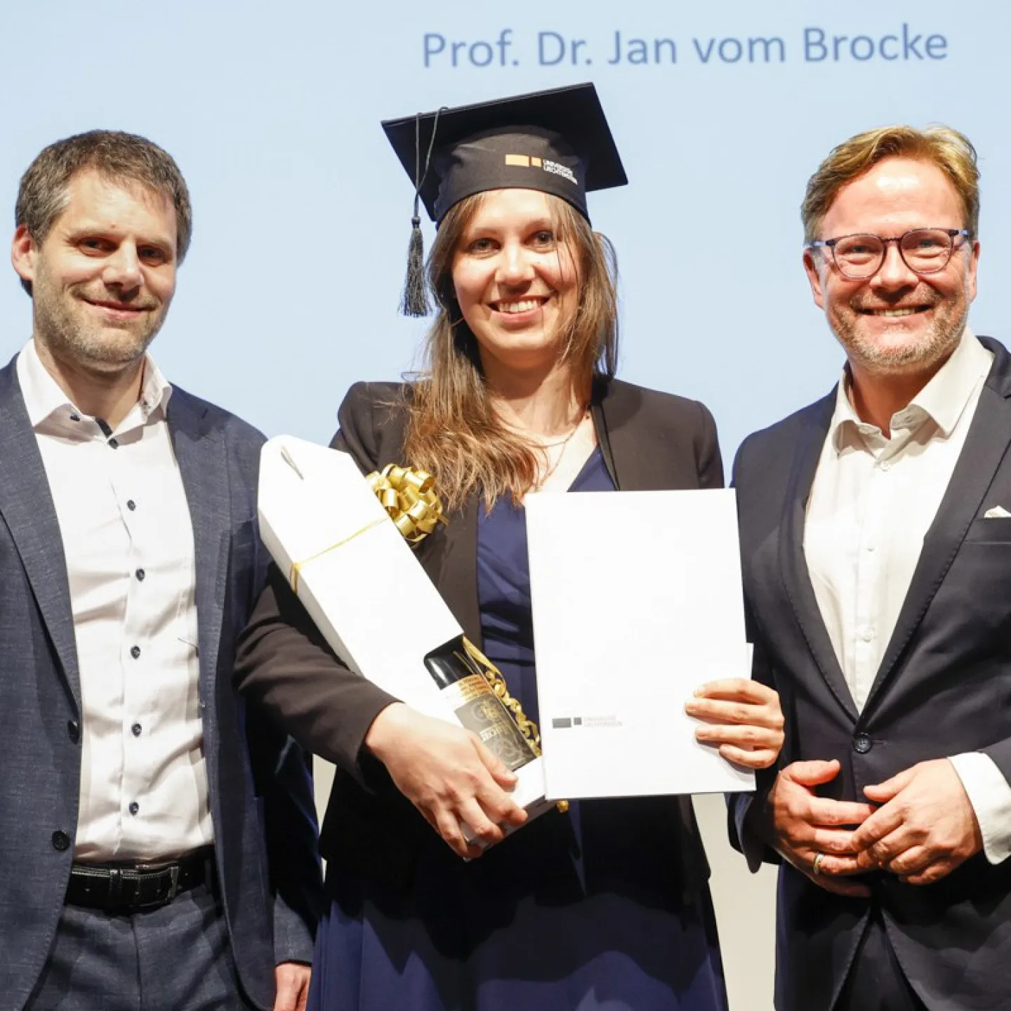 Dr. Christian Frommelt und Prof. Dr. Jan vom Brocke neben Dr. Amandine Herbé mit ihrem Diplom.