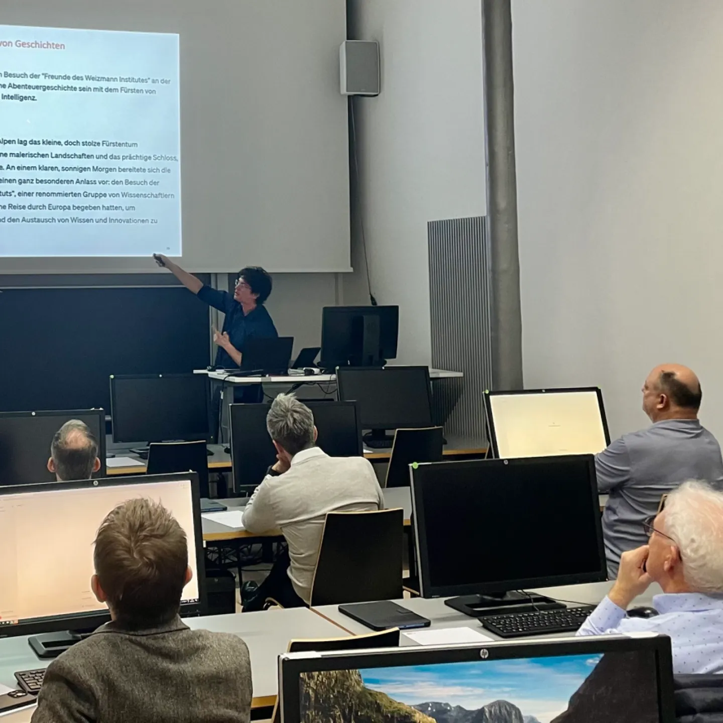 Ein Dozent hält einen interaktiven Workshop an der Universität Liechtenstein. Er zeigt auf eine Präsentation über künstliche Intelligenz, während die Teilnehmenden an Computern sitzen und aufmerksam zuhören.