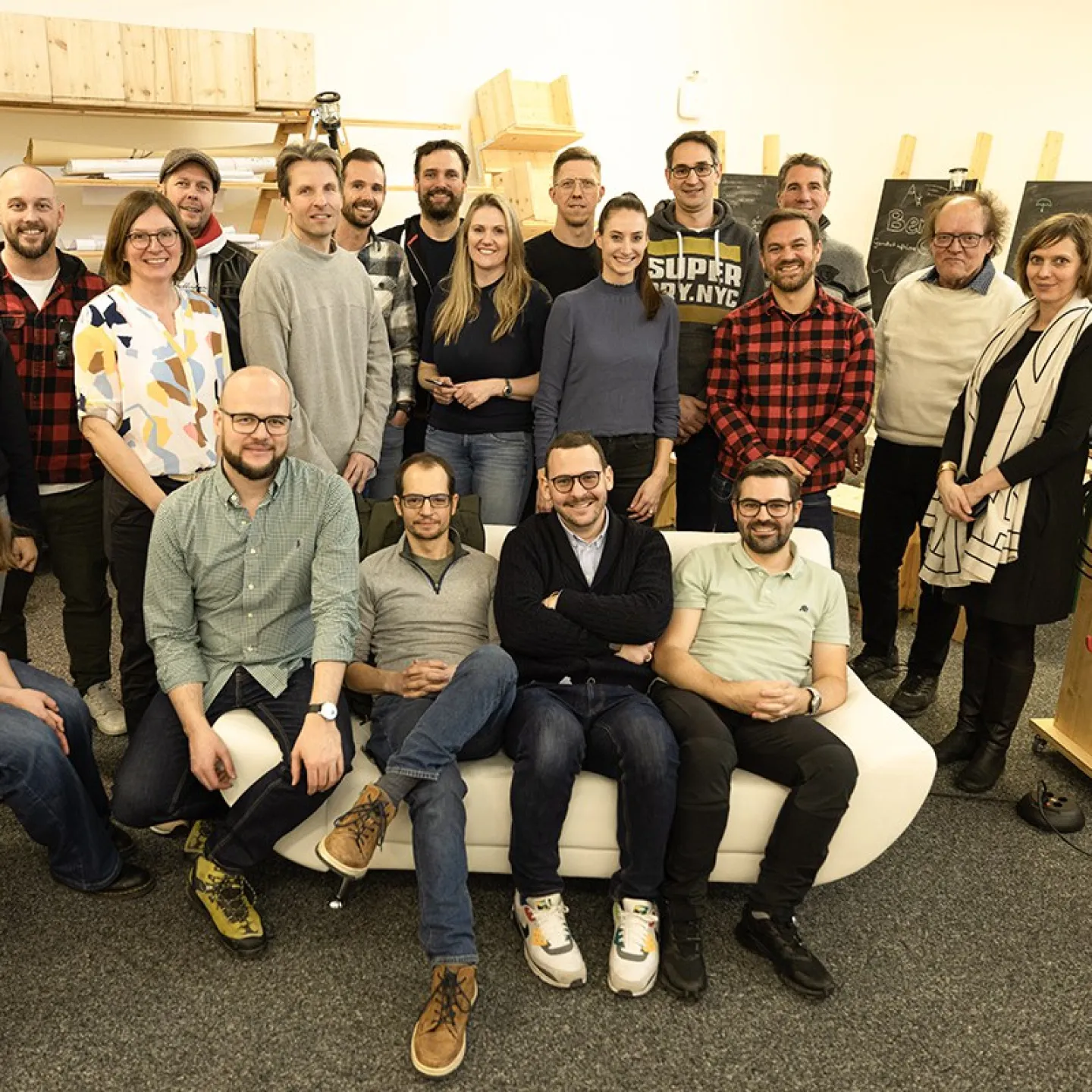 Gruppenfoto von Absolventen des Masterprogramms in Entrepreneurship der Universität Liechtenstein, die sich in einem Raum mit Regalen und Tafeln versammelt haben. Die Personen lächeln und stehen oder sitzen in zwei Reihen.