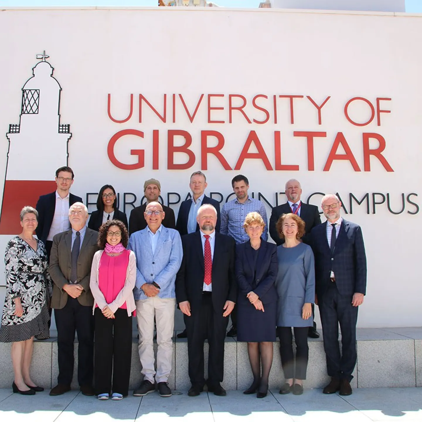 Eine Gruppe von Personen steht vor einem Gebäude mit der Aufschrift "University of Gibraltar". Sie posieren für ein Gruppenfoto bei sonnigem Wetter.
