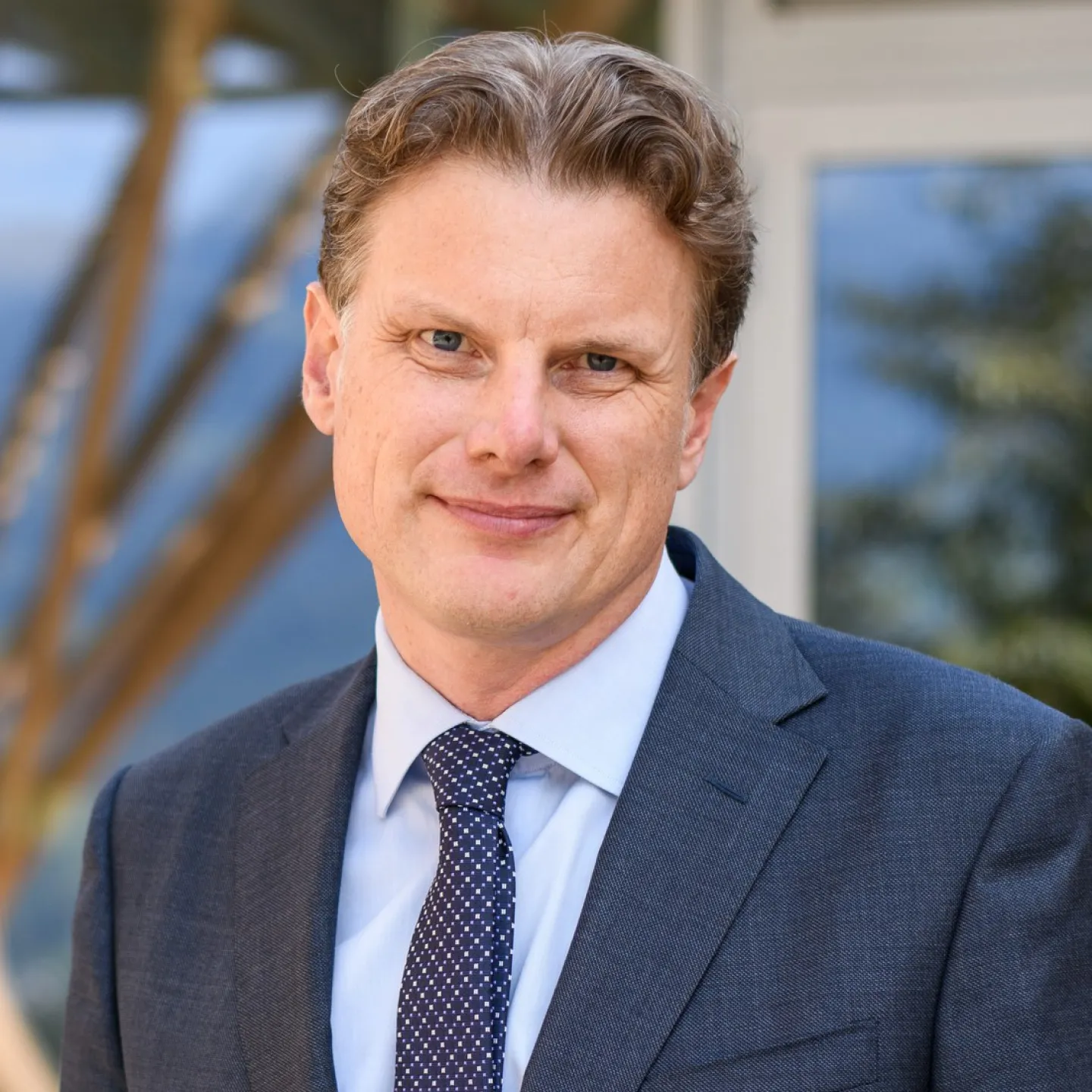 Ein Mann in einem Anzug steht lächelnd vor einem Gebäude.