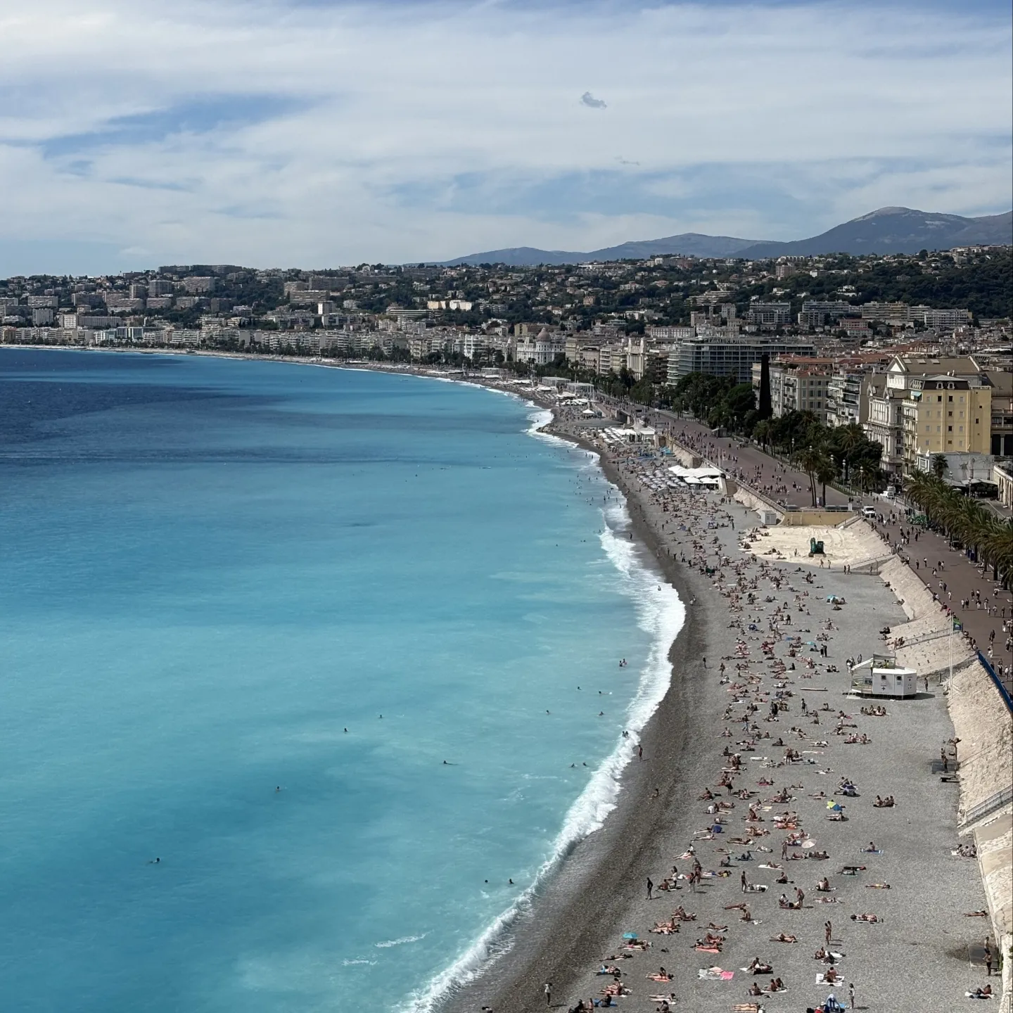 Grau wirkender Strand mit Blauem Wasser und vielen Menschen