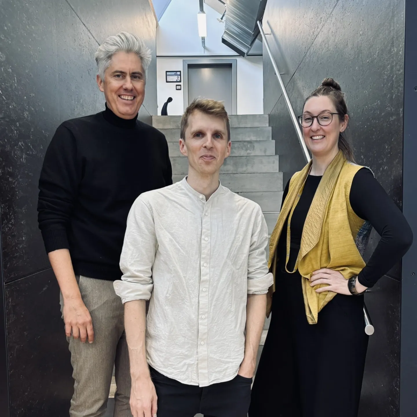 Drei Personen auf einer grau/schwarzen Treppe