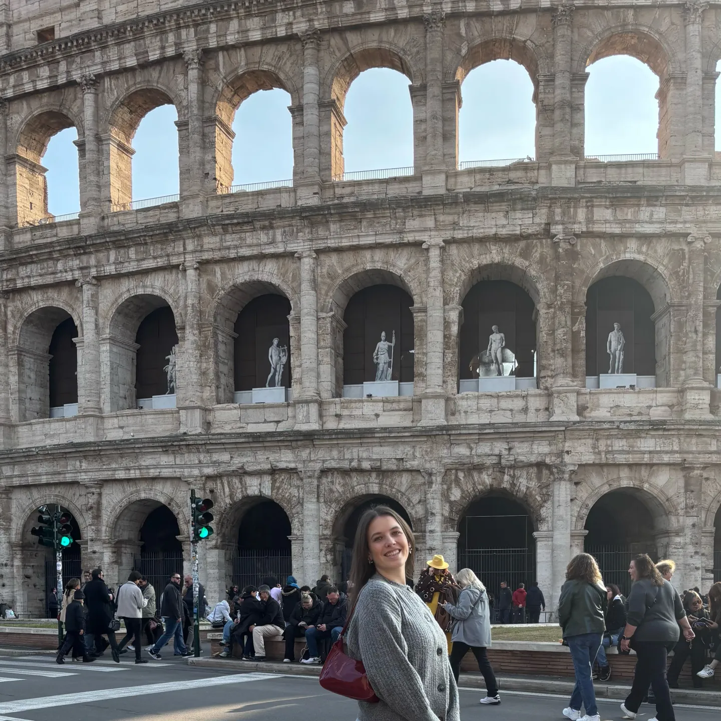 Frau steht lächelnd vor dem Kolosseum, während im Hintergrund Touristen an der Straße entlanggehen.