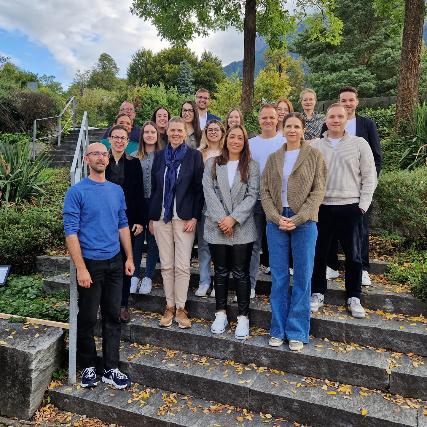 Gruppe von Erwachsenen steht auf Treppe in grüner Umgebung.