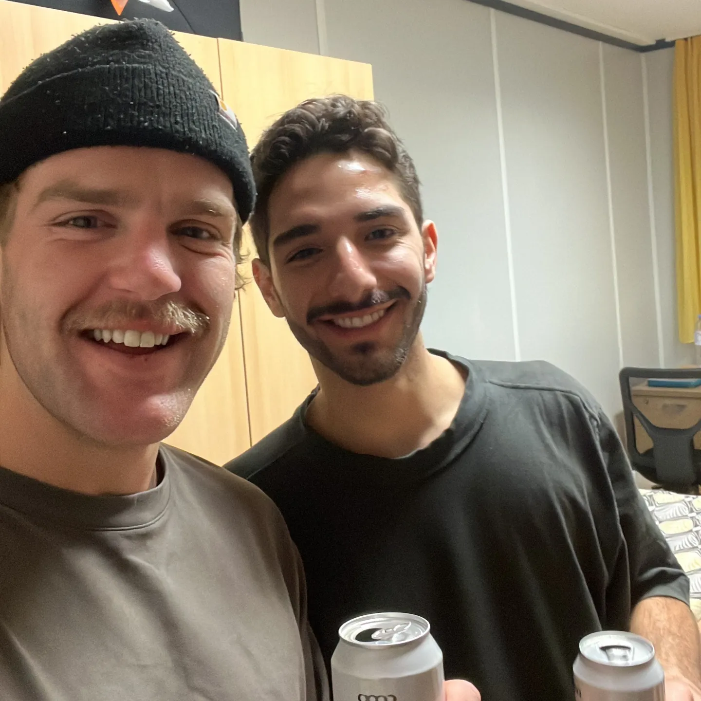 Zwei Studierende halten lächelnd Getränkedosen in die Kamera.