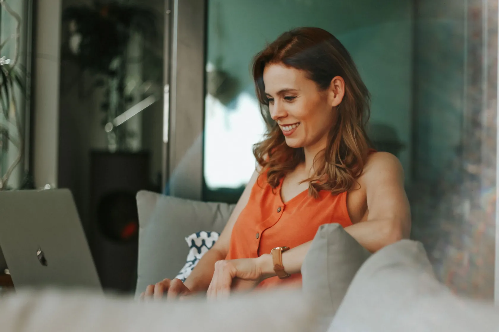 Eine Frau sitzt auf einem Sofa und arbeitet am Laptop.