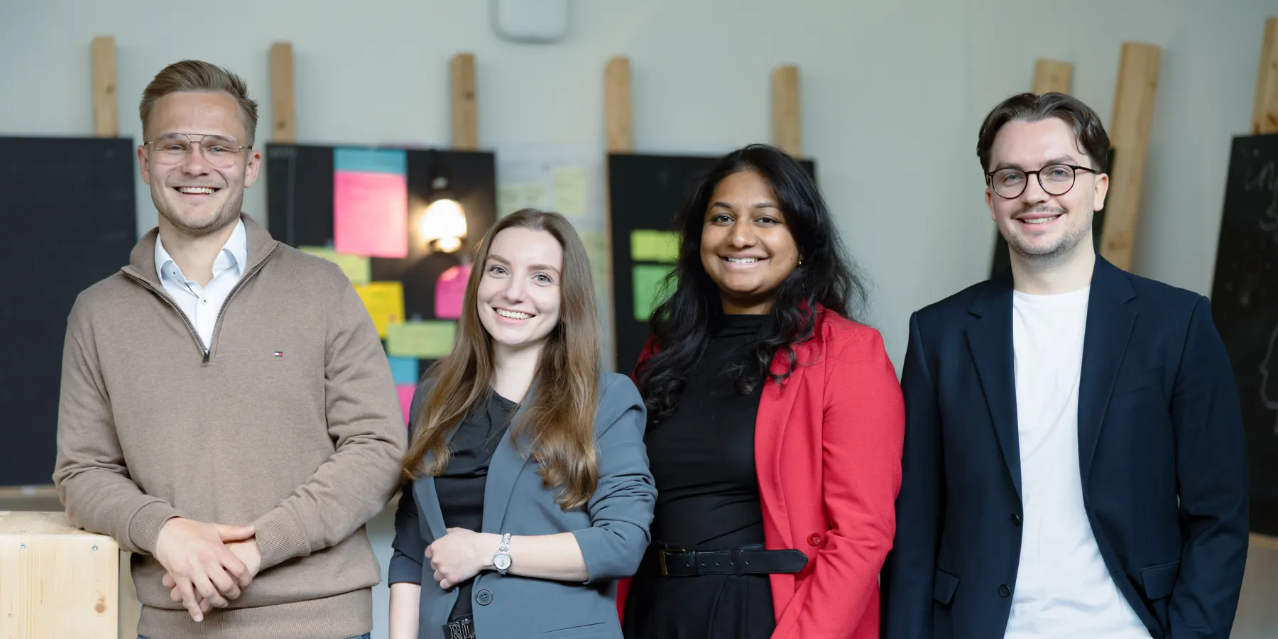 Vier Studierende des Master Entrepreneurship, Innovation und Leadership der Universität Liechtenstein posieren gemeinsam im modernen Campusgebäude – Fokus auf studentische Vielfalt und Gemeinschaft.