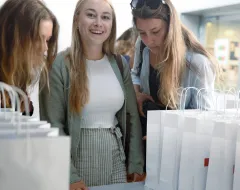 Drei neue Studentinnen stehen am Campus der Universität Liechtenstein am Welcome Day vor einem Stapel von Taschen
