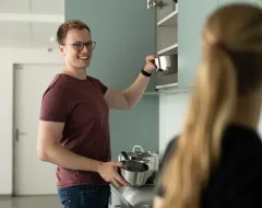 Student stellt eine Metallschüssel in den Küchenschrank der Gemeinschaftsküche des Studierendenwohnheims der Universität Liechtenstein.