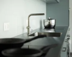 Detailaufnahme der Küchenspüle mit Edelstahlarmatur und Kochgeschirr in der Gemeinschaftsküche des Studierendenwohnheims.