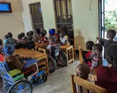 Kinder sitzen in einem Raum und schauen auf einen Fernseher.