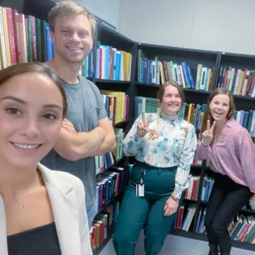 Fünf Mitglieder des International Office der Universität Liechtenstein posieren lachend vor einem Bücherregal in einer Bibliothek.