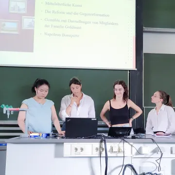 Vier Studentinnen der Universität Liechtenstein halten gemeinsam eine Präsentation zu kunsthistorischen Themen im Hörsaal.