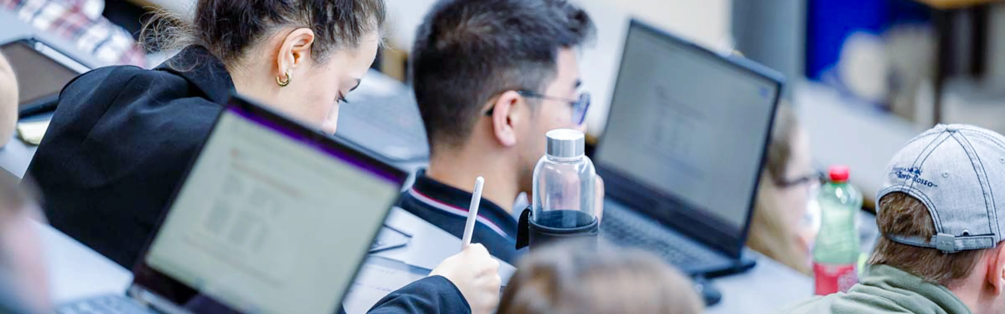 Studierende der Universität Liechtenstein arbeiten konzentriert mit Laptops im Hörsaal und machen sich Notizen.