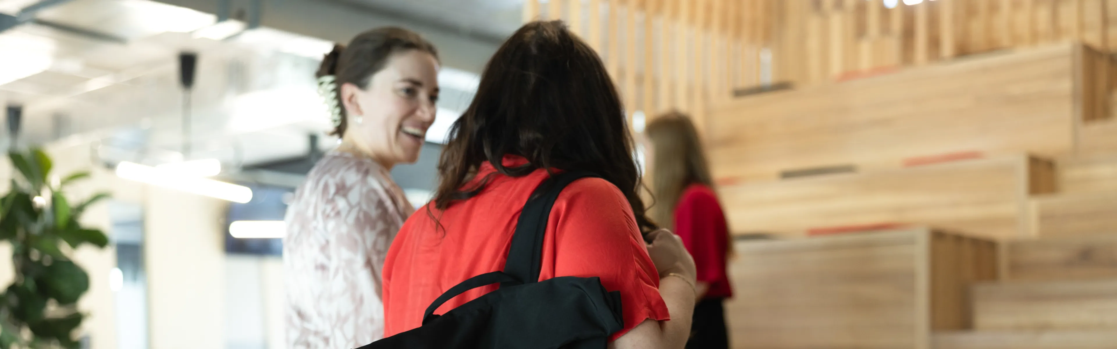 Studierende mit Uni-Rucksack stehen vor den Sitzstufen, im Hintergrund entspannte Gesprächsszene.