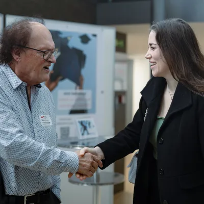Professor der Universität Liechtenstein begrüßt eine junge Alumna mit einem Handschlag im Eingangsbereich der Universität.