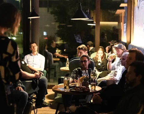 Alumni-Treffen in gemütlicher Atmosphäre: Eine Gruppe von Menschen sitzt in einer Lounge, unterhält sich und genießt Getränke.