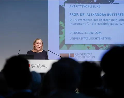 Eine Person hält eine Antrittsvorlesung im Auditorium der Universität Liechtenstein. Im Hintergrund ist eine Präsentationsfolie mit dem Titel der Vorlesung und dem Datum zu sehen. Das Publikum sitzt im Vordergrund.