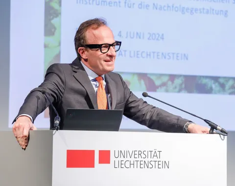 Ein Redner steht an einem Podium der Universität Liechtenstein und hält eine Präsentation. Im Hintergrund ist ein Bildschirm mit dem Datum 4. Juni 2024 zu sehen.