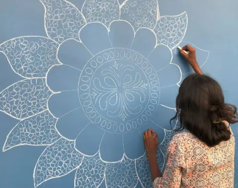 Eine Person zeichnet ein detailliertes, weißes Mandala-Muster auf eine blaue Wand.