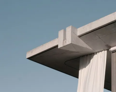 Betonvordach mit klaren Linien und hängendem weißen Vorhang vor blauem Himmel. Moderne Architektur, die Minimalismus und Eleganz vereint.