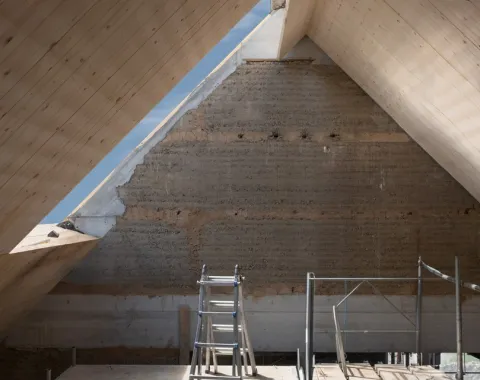 Innenansicht eines Dachbodens in Renovierung mit sichtbarer Holzkonstruktion und Gerüst. Natürliches Licht fällt durch ein Dachfenster.