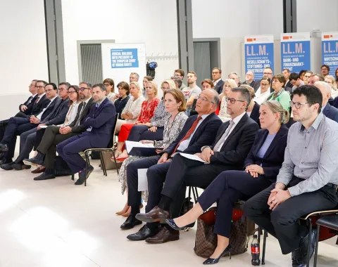 Eine Gruppe von Menschen sitzt in einem Konferenzraum der Universität Liechtenstein. Sie hören aufmerksam einem Vortrag zu. Im Hintergrund sind Banner mit der Aufschrift "LL.M." zu sehen.