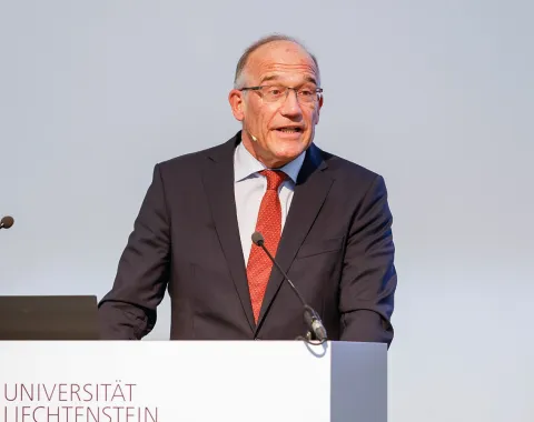 Ein Redner im Anzug steht am Podium der Universität Liechtenstein und hält eine Präsentation.