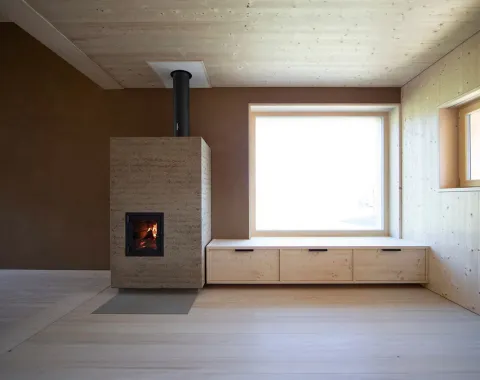 Ein modernes, minimalistisches Wohnzimmer mit einem Holzofen, einer großen Fensterbank und Holzwänden, gestaltet von EMM Architekten.