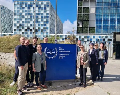 Gruppe von Studierenden des Executive Master of Laws (LL.M.) im Wirtschaftsstrafrecht vor dem Internationalen Strafgerichtshof in Den Haag, lächelnd und posierend vor dem Gebäude mit dem Logo des Gerichtshofs.